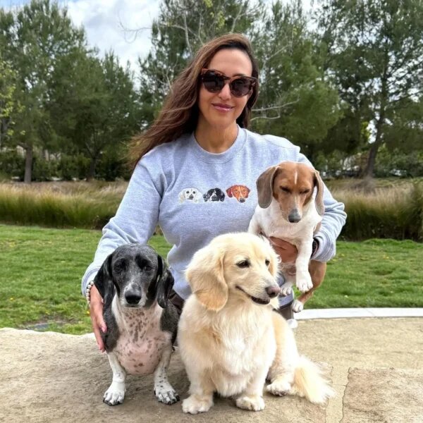 Woman wearing custom embroidered sport grey sweatshirt featuring three dachshund dog portraits while holding her three dogs in a park