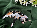 Detailed close-up of custom embroidered tricolor calico cat with fine whiskers and paws on forest green fabric