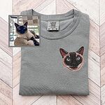 Custom embroidered dark cat portrait on a gray T-shirt beside the original pet photo