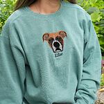 Model wearing sage green garment-dyed crewneck sweatshirt with custom embroidered boxer dog face and name Ellie stitched on center chest