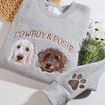 Sport grey crewneck sweatshirt flat lay with white flowers featuring custom embroidered two doodle dog portraits named Cowboy and Posie and sleeve paw print