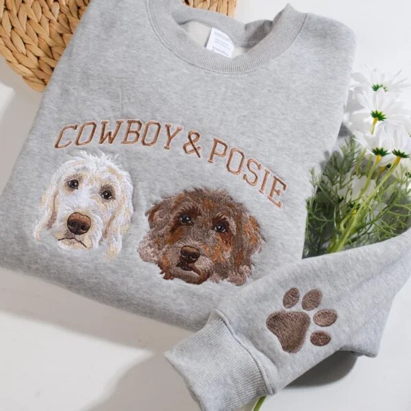 Sport grey crewneck sweatshirt flat lay with white flowers featuring custom embroidered two doodle dog portraits named Cowboy and Posie and sleeve paw print