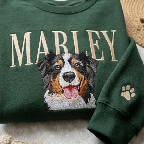 Close-up of a green custom embroidered dog portrait sweatshirt with the name Marley and paw print sleeve