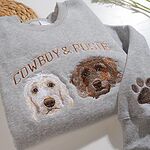 Detailed close-up of custom embroidered cream and brown doodle dog faces with Cowboy and Posie lettering and embroidered paw on sleeve cuff