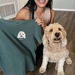 Smiling customer holding dark green custom embroidered pet portrait t-shirt with stitched dog face next to her real golden doodle