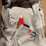 Sport grey sweatshirt showing custom embroidered equestrian rider in red jacket on white horse with personalized sleeve name Jodie and winged horseshoe