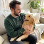 Dog dad wearing a forest green sweatshirt with an embroidered Golden Retriever portrait while holding his dog