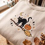 Close-up view of detailed thread embroidery showing a black cat, crescent moon, stars, and pumpkin on broom