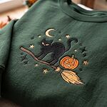 Forest green sweatshirt showing detailed embroidery of a black cat riding a broom with a smiling jack-o-lantern pumpkin