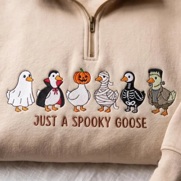 Close-up embroidery detail showing six geese in Halloween costumes including Ghost, Dracula, Pumpkin, Mummy, Skeleton, and Frankenstein