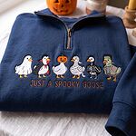 Deep navy blue quarter zip sweater folded near a carved pumpkin with white and colorful embroidered geese
