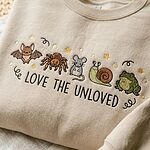 Close-up stitch detail of embroidered bat, tarantula spider, mouse, snail, frog, and Love The Unloved lettering