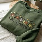 Folded dark forest green sweatshirt with embroidered Love The Unloved creatures design on textured linen
