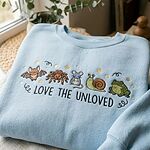 Light blue chambray sweatshirt with embroidered Love The Unloved retro biology graphic flatlay by window
