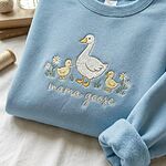 Pastel light blue sweatshirt folded on white fabric featuring embroidered Mama Goose and goslings design