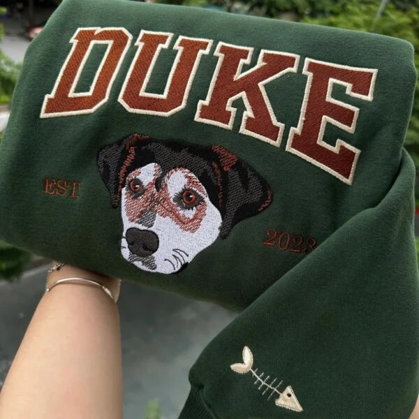Forest green custom dog portrait varsity sweatshirt embroidered with Duke name, EST. 2023, and fishbone sleeve icon