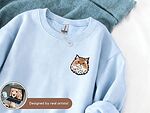 Light blue sweatshirt with a custom embroidered cat portrait and artist design preview