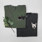 Two folded shirts showing two custom embroidered cats on green fabric and a dog face on charcoal fabric