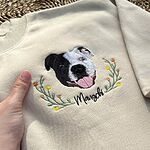 Personalized black and white dog face embroidery with pet name on a cream sweatshirt