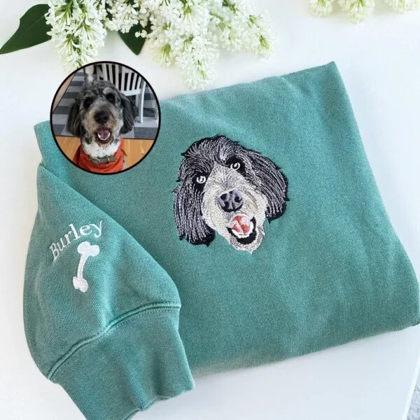 Embroidered fluffy dog portrait on sage green crewneck featuring personalized sleeve embroidery with pet name Burley and dog bone design