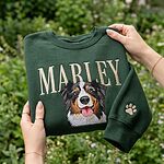 Personalized green pet portrait embroidered sweatshirt held outdoors with Marley name and paw print