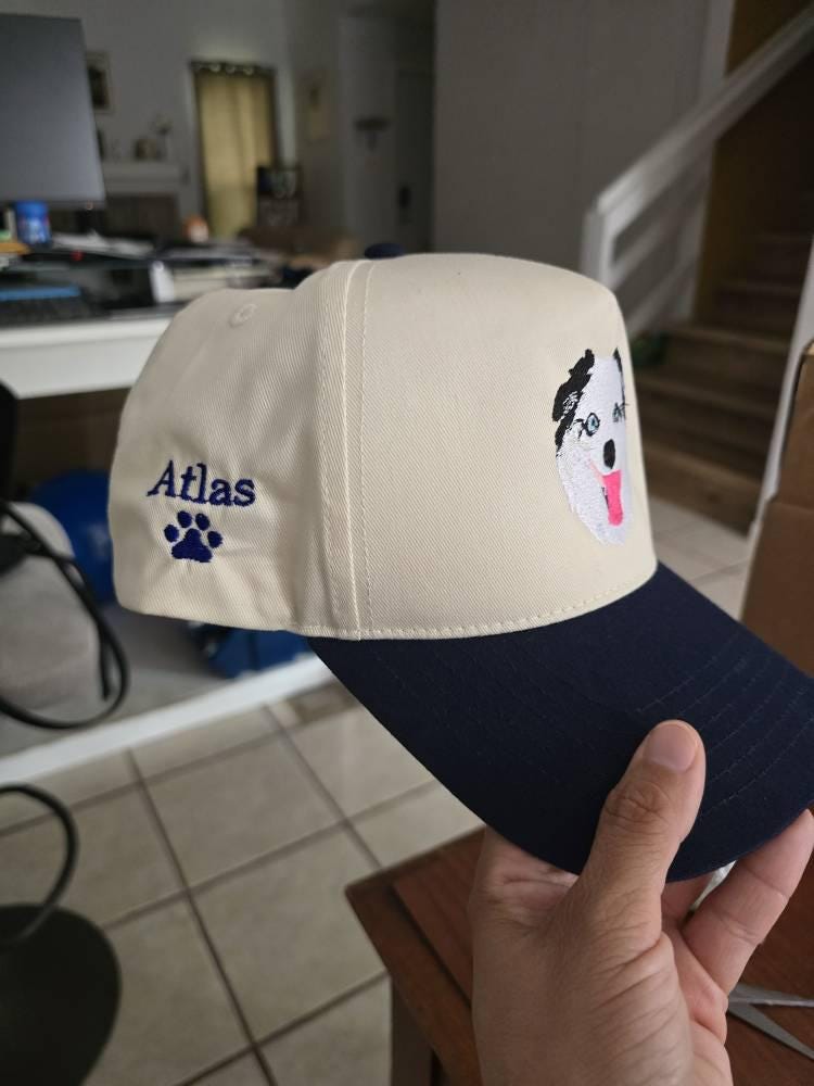 Customer photo of a cream and navy cap with a black-and-white embroidered dog portrait, side name and paw print