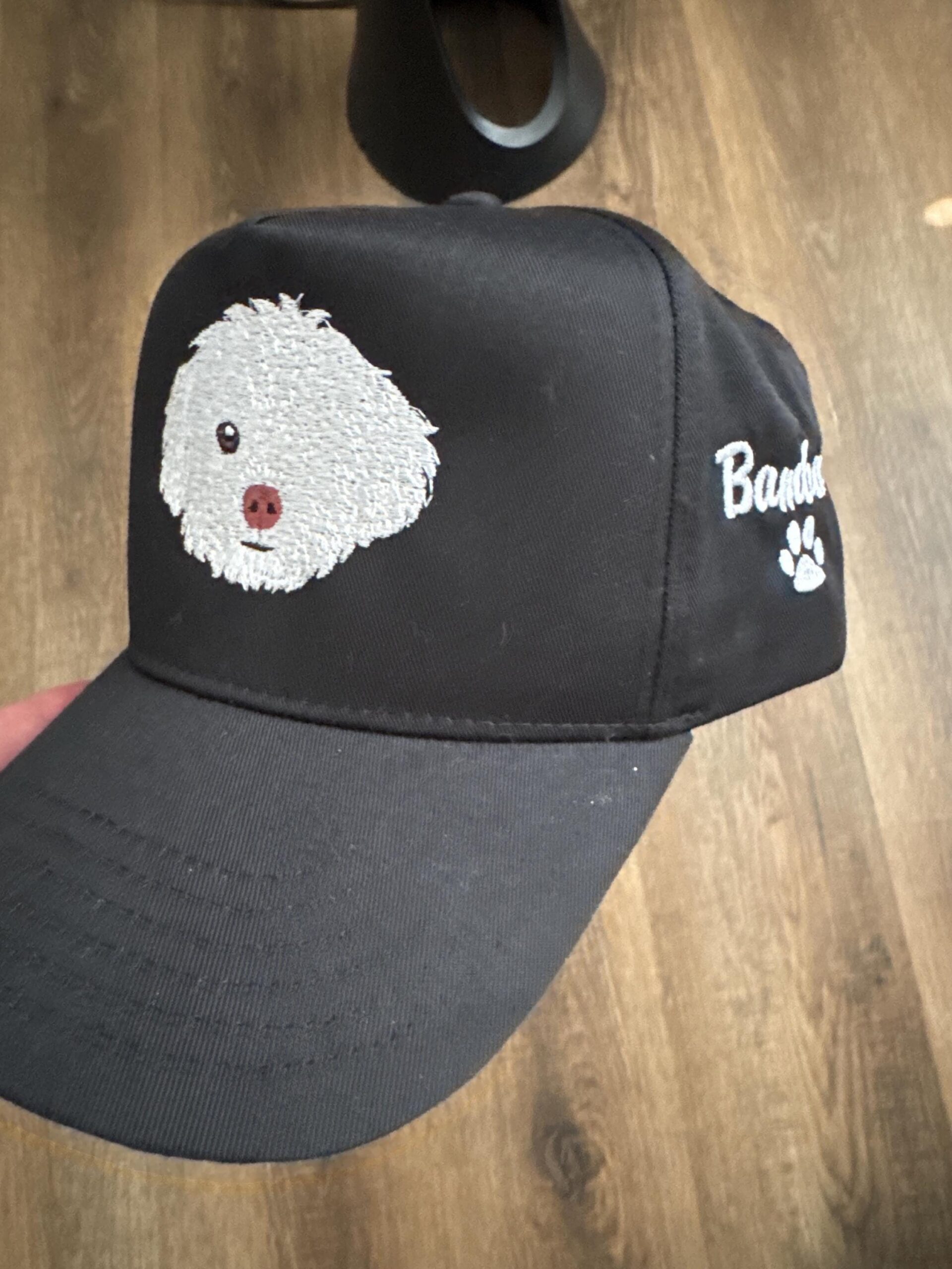 Customer photo of a black cap with a white embroidered dog portrait, side name and paw print