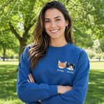 Happy smiling woman with arms crossed in a sunny green park wearing a custom blue Cat Mom sweatshirt with embroidered cat portraits and names