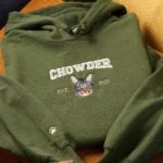 Forest green custom embroidered pet portrait hoodie neatly folded on textured yellow armchair showing Chowder arch text and cat portrait