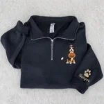 Folded black quarter zip fleece pullover featuring embroidered Bernese Mountain Dog in witch hat holding pumpkin basket with personalized Burger sleeve embroidery on white fur rug
