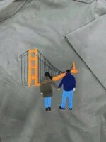 Olive green custom embroidered t-shirt showing a couple holding hands in front of the orange Golden Gate Bridge embroidered from travel photo