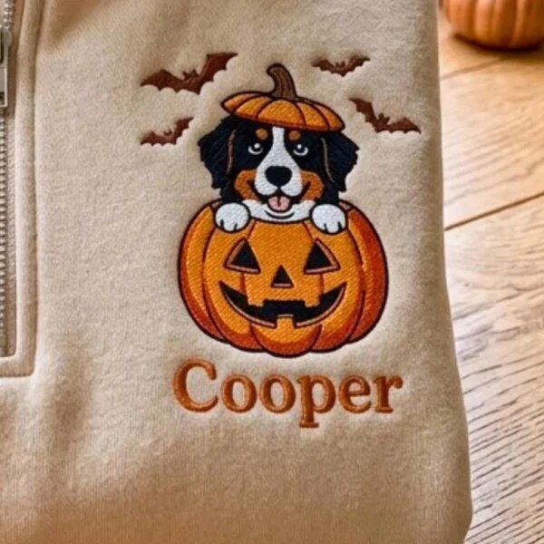 Detailed macro close-up of vibrant embroidery showing dog portrait in a jack-o-lantern pumpkin with bats and Cooper text on textured fleece