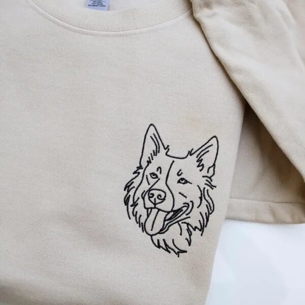Folded sand beige fleece crewneck sweatshirt featuring custom black thread embroidered dog face portrait on the left chest