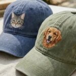 Detailed macro close-up of embroidery stitching showing tabby cat face on blue cap and golden retriever dog face on olive green washed hat