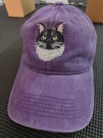 Purple vintage washed cotton baseball cap featuring artisanal embroidered black and white tuxedo cat face with green eyes and white chest fur