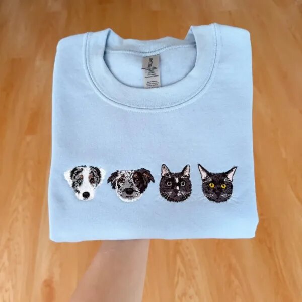 Folded Carolina blue fleece crewneck sweatshirt featuring custom realistic multi-color embroidery of four pet portraits with two dogs and two cats across chest