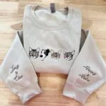 Sand beige crewneck sweatshirt with four embroidered pet portraits across chest and personalized pet names Joey, Cleo, Poppy, and Pietro on sleeves