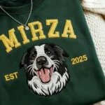 Detailed macro close-up of embroidered border collie dog face and yellow 3D satin stitch varsity lettering Mirza on dark green fleece
