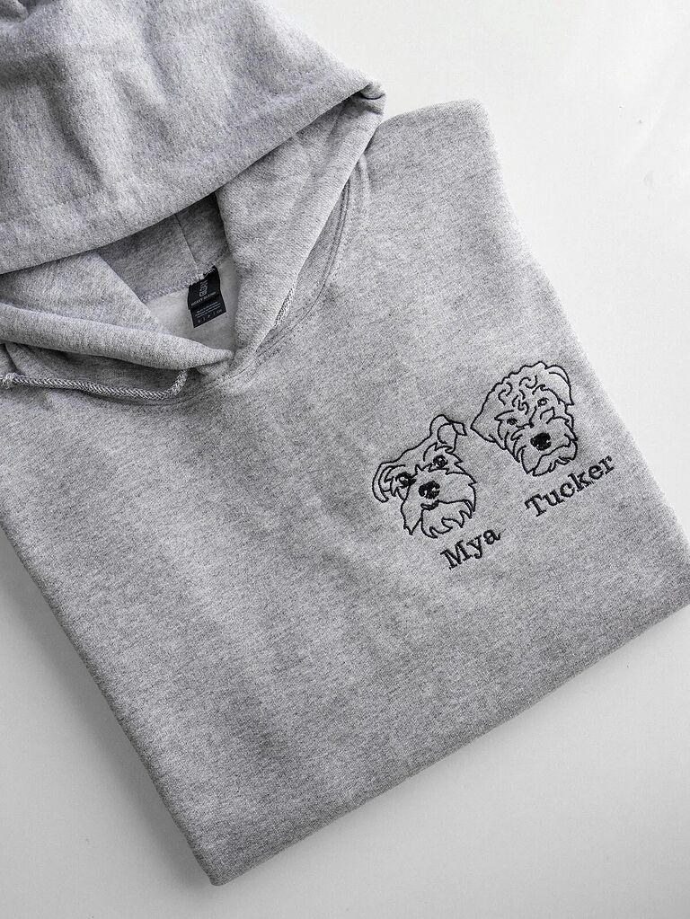Folded heather ash grey fleece hoodie featuring custom black thread embroidered portraits of two dogs with personalized names Mya and Tucker
