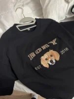 Black crewneck sweatshirt on a hanger, embroidered with a dog portrait, the name Rory and EST 2016