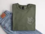 Folded military green crewneck sweatshirt styled with blue jeans featuring delicate white thread embroidered loafing cat portrait on left chest