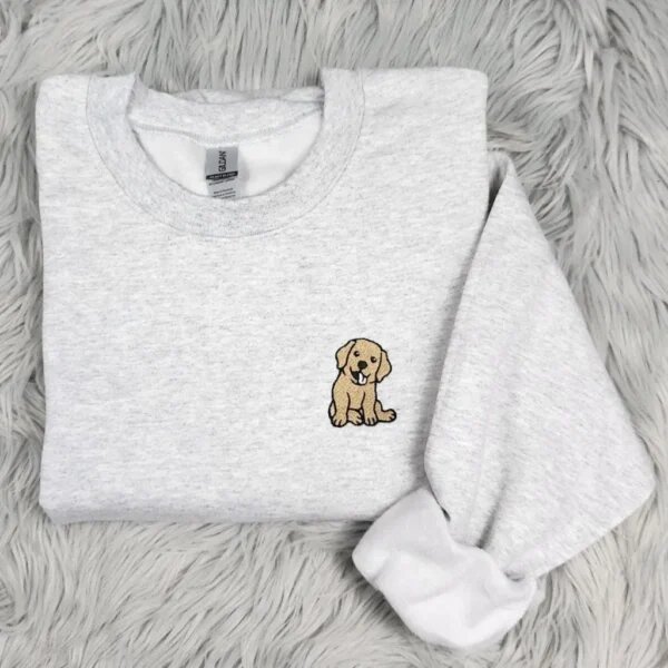 Folded ash heather grey fleece crewneck sweatshirt featuring a cute smiling golden labrador retriever puppy embroidered on left chest resting on grey faux fur rug
