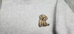 Macro close-up view of textured thread embroidery showing a golden labrador retriever puppy with pink tongue and black outline on heather grey sweatshirt fleece