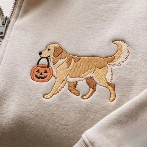 Close-up macro shot of dense embroidery stitching showing Golden Retriever carrying a smiling jack-o-lantern bucket on sand fleece sweater fabric