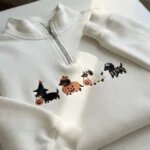 Folded white fleece quarter zip pullover featuring four embroidered Halloween dachshund dogs dressed as a witch, pumpkin, ghost, and skeleton