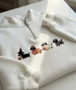 Folded white fleece quarter zip pullover featuring four embroidered Halloween dachshund dogs dressed as a witch, pumpkin, ghost, and skeleton