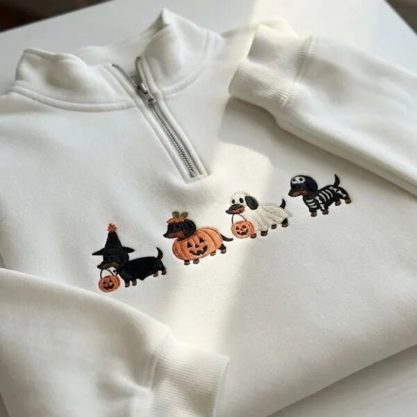 Folded white fleece quarter zip pullover featuring four embroidered Halloween dachshund dogs dressed as a witch, pumpkin, ghost, and skeleton