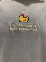 Detailed macro view of sleepy pixel chicken embroidery and crisp lettering on soft steel blue textured fabric