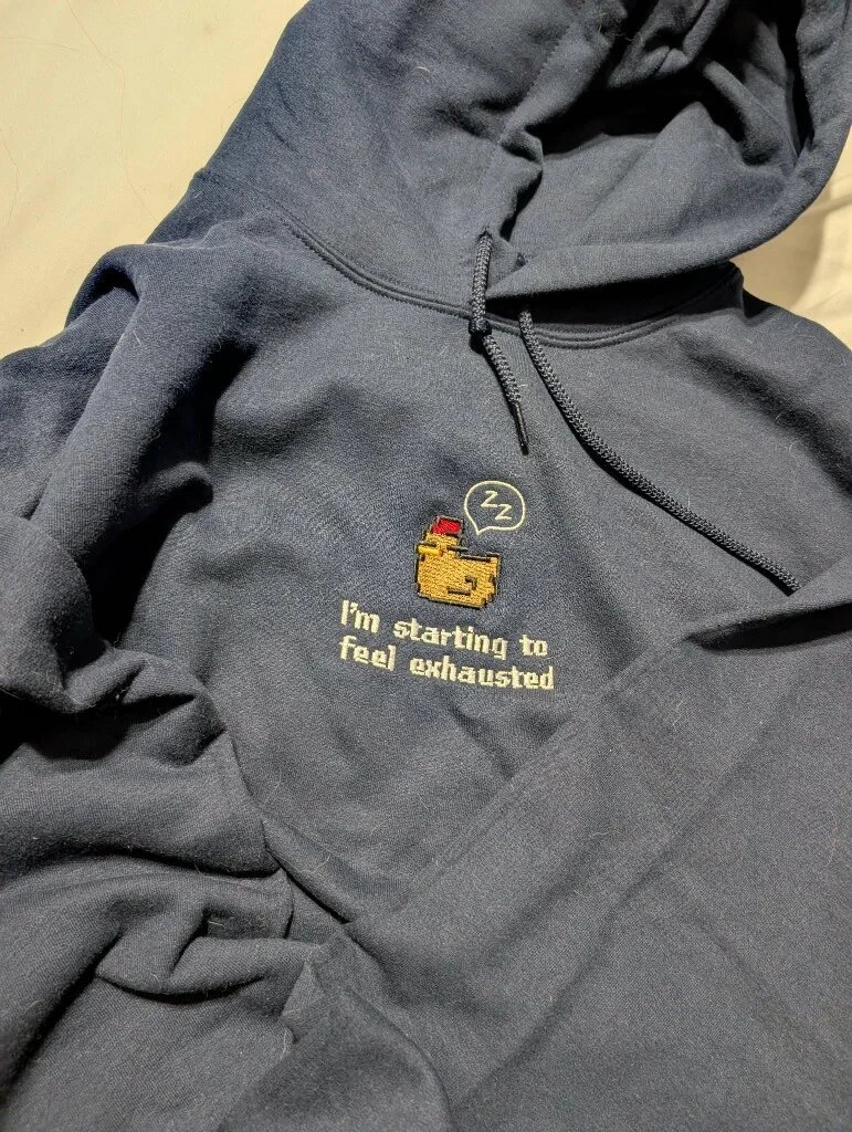 I'm Starting to Feel Exhausted Embroidered Hoodie – Navy Blue Flatlay Navy blue pullover embroidered hoodie with drawstrings displaying centered sleepy pixel chicken and tired quote embroidery