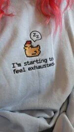 Close-up view of light blue embroidered crewneck sweatshirt worn with sleepy chicken and I'm starting to feel exhausted quote